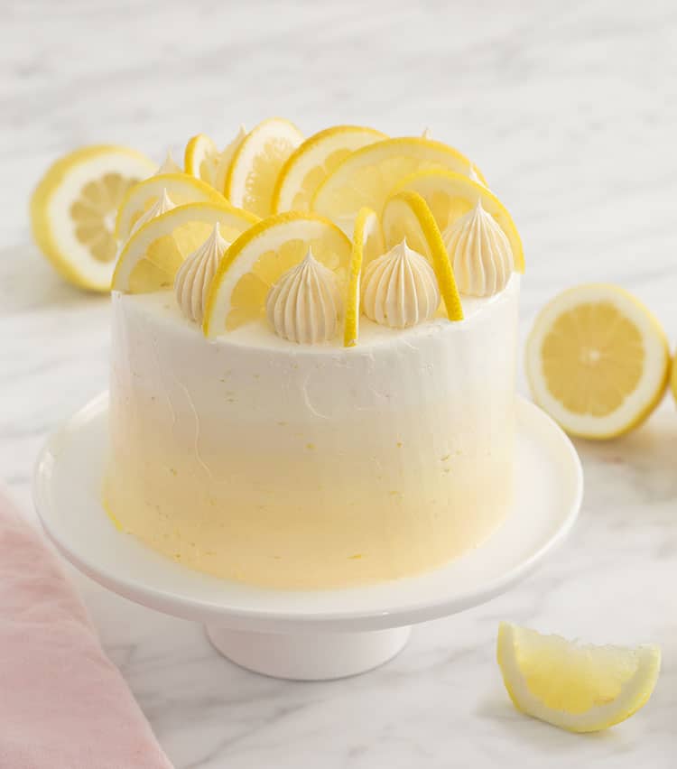 A yellow ombré lemon cake topped with dollops and lemon slices.