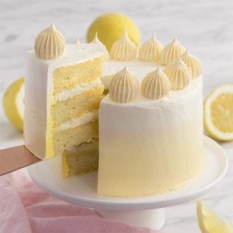a lemon cake on a white cake stand with a piece being removed.