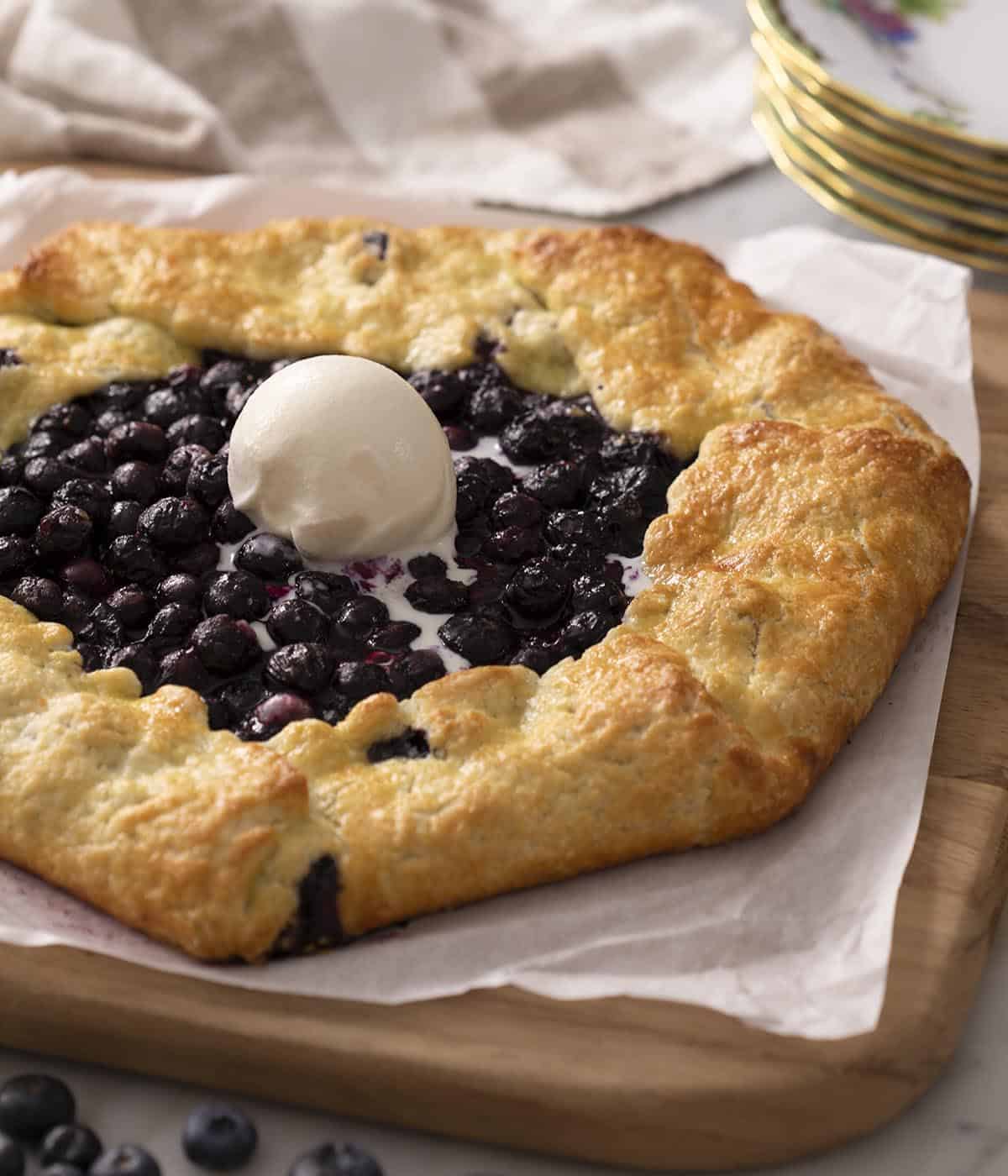 A closeup photo of a blueberry galette with a scoop of vanilla ice cream on top.