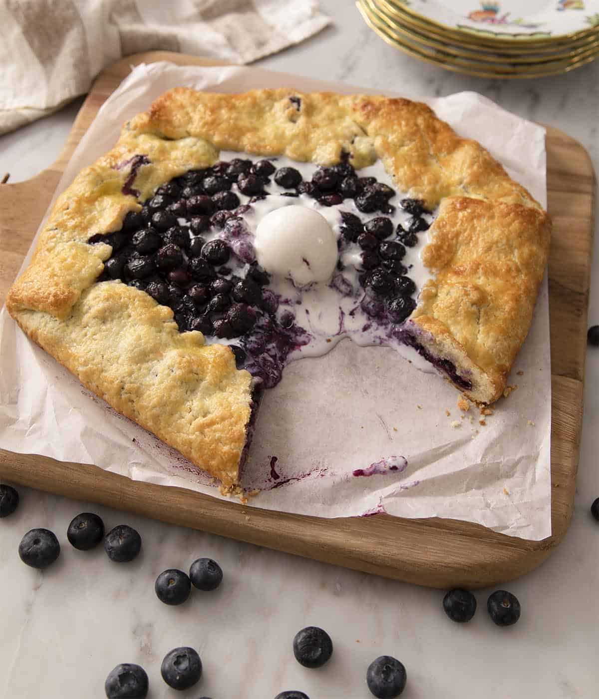 A blueberry galette on a wooden cutting board with a piece removed.