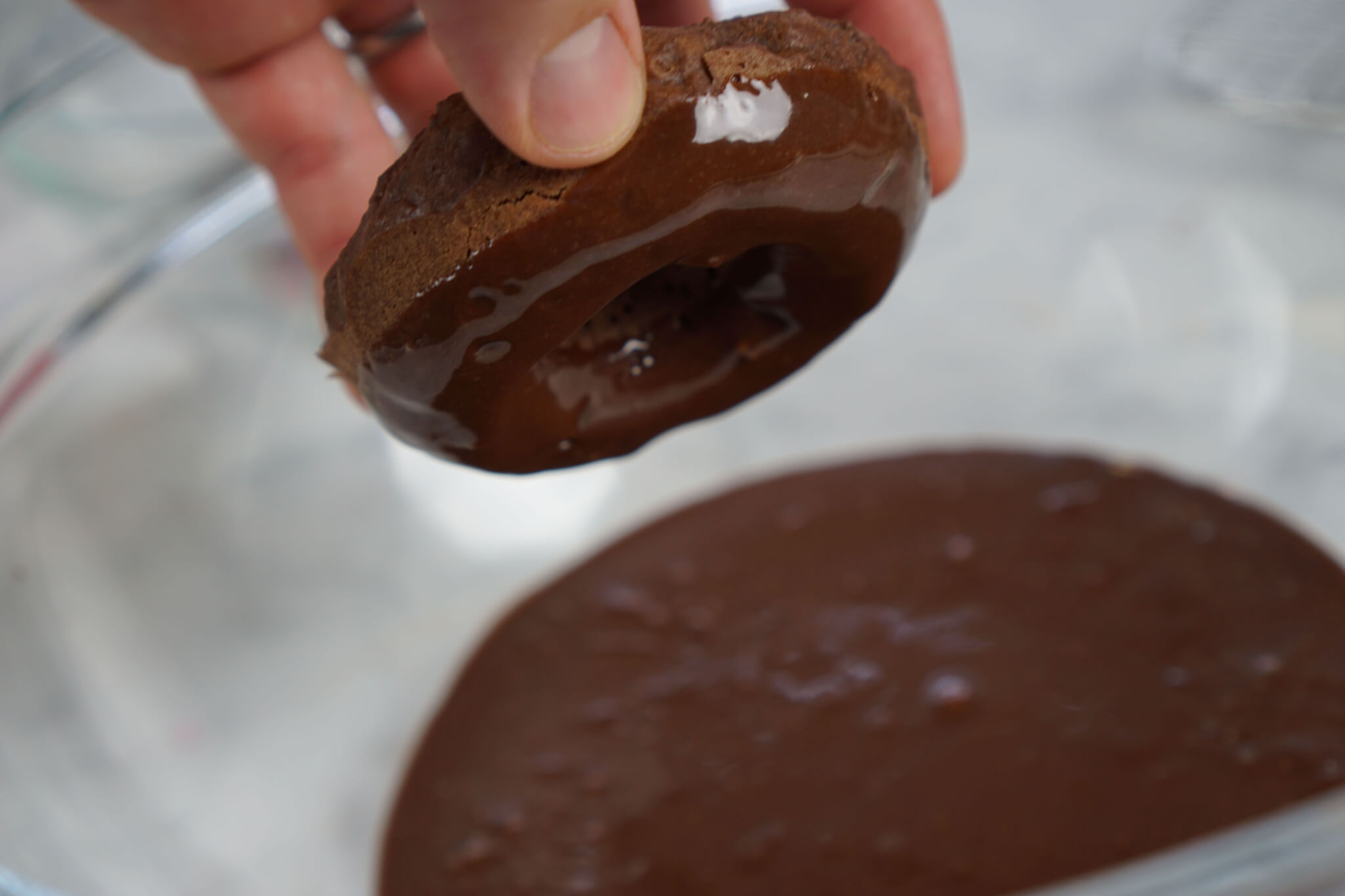 Chocolate donut getting dipped into ganache