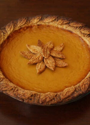 A photo of a pumpkin pie with leaves made from pie crust decorated on the middle of the cake