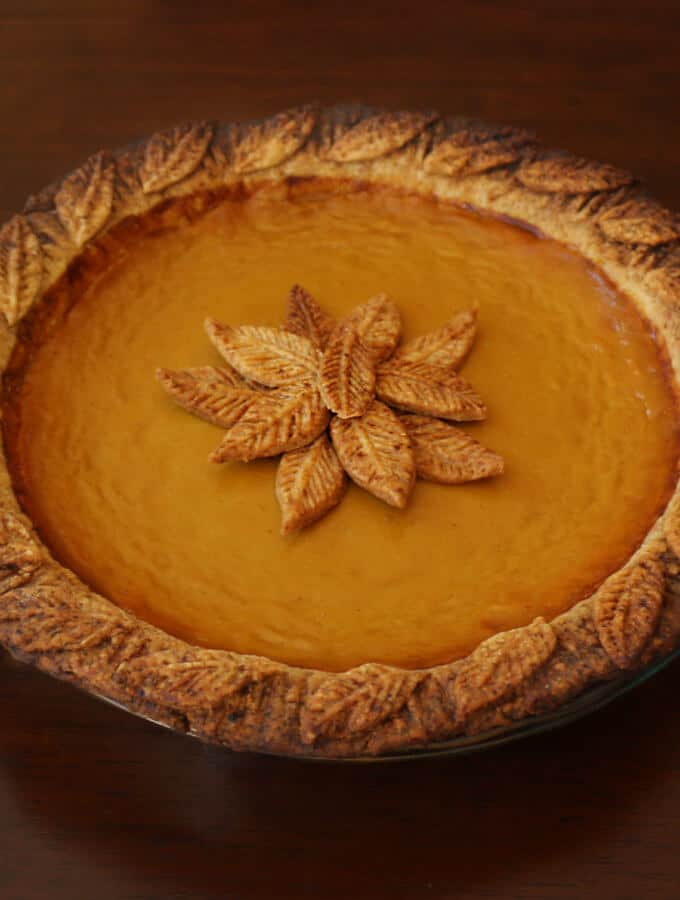 A photo of a pumpkin pie with leaves made from pie crust decorated on the middle of the cake