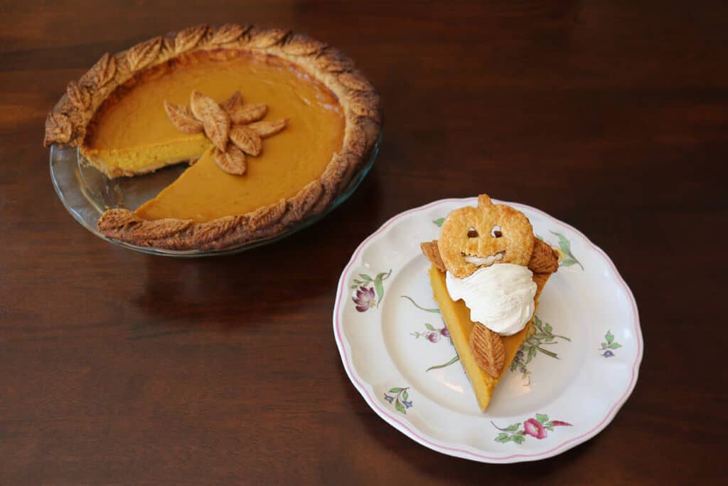 A photo of pumpkin pie with a slice removed and on a plate served with whipped cream.