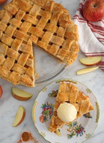 A top town photo of an apple pie with a lattice top and a piece on a plate.