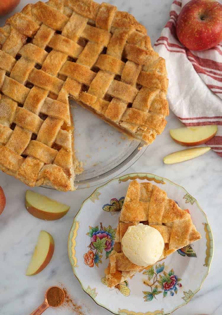 A top town photo of an apple pie with a lattice top and a piece on a plate.