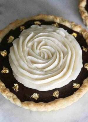 A photo of a chocolate tart topped with a spiral of buttercream and decorated with edible gold leaf.