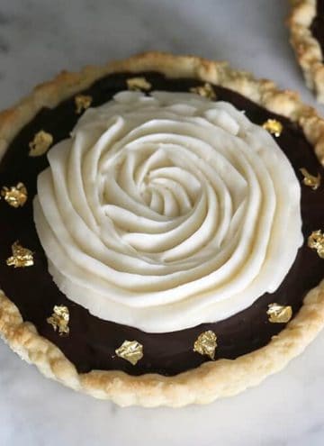 A photo of a chocolate tart topped with a spiral of buttercream and decorated with edible gold leaf.