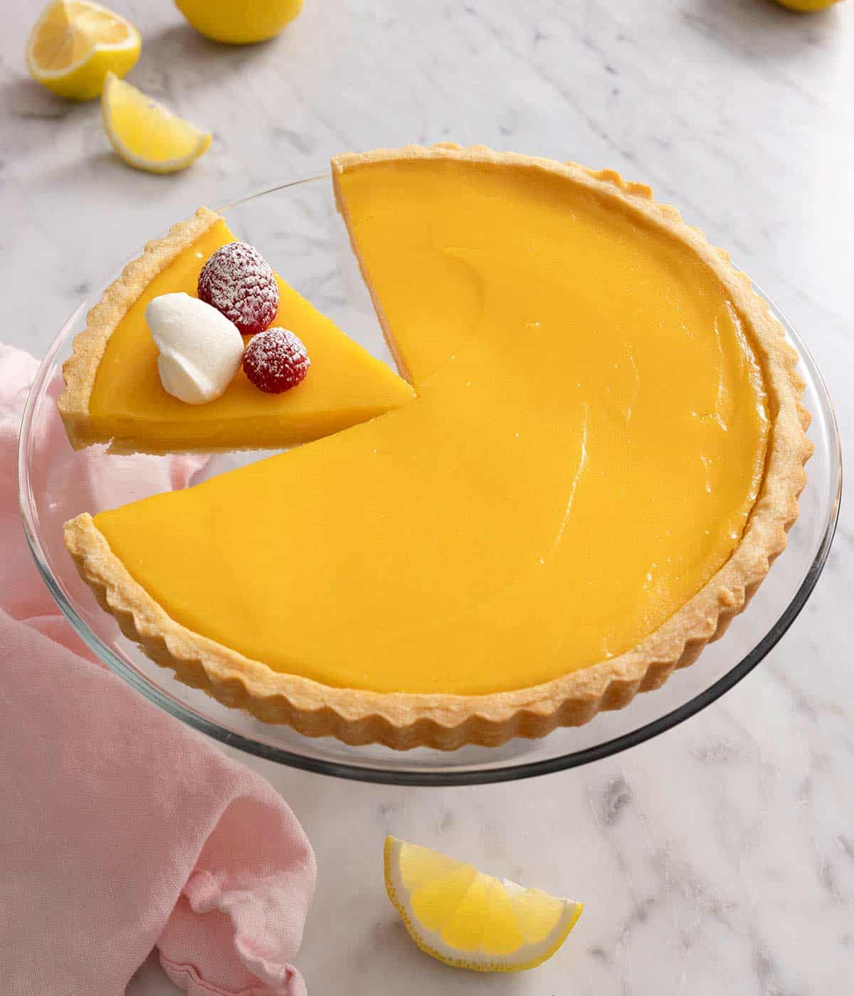 A lemon tart on a cake stand with a slice cut