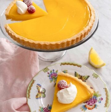 A lemon tart on a cake stand with a slice plated in front.