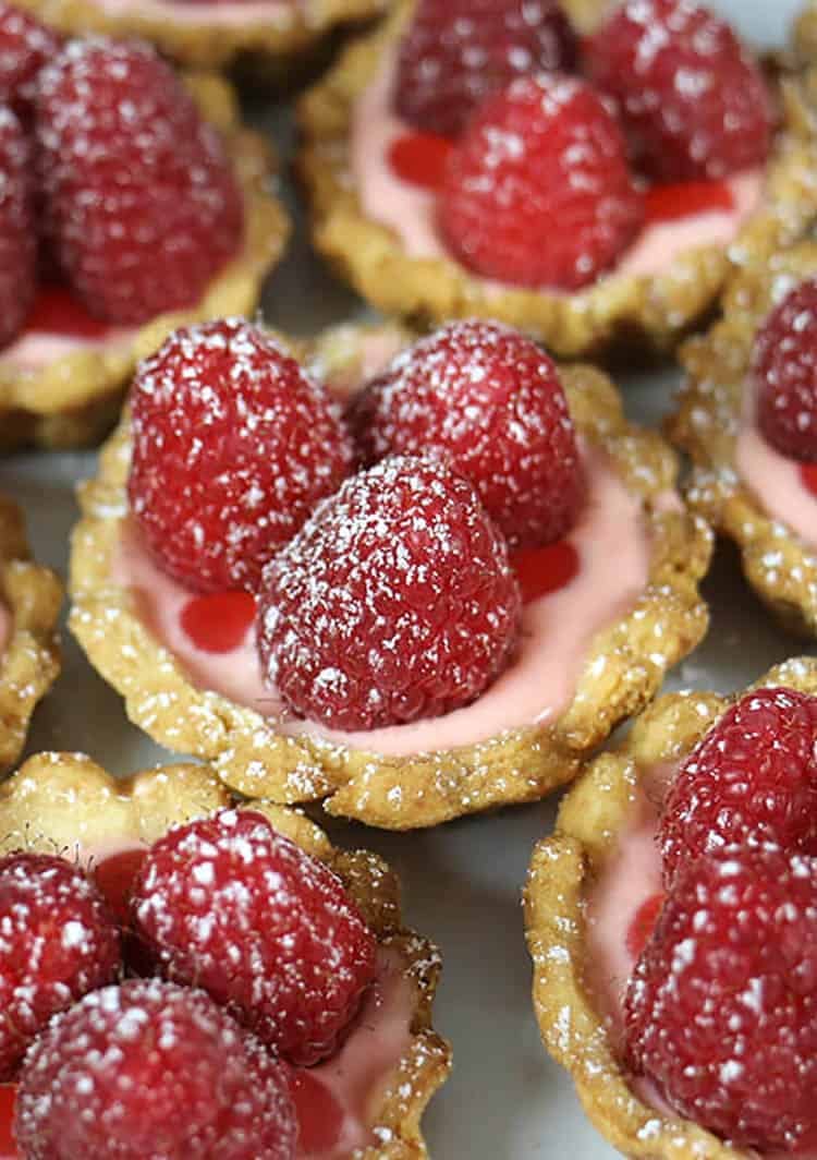 a group of small raspberry tarts dusted with powdered sugar