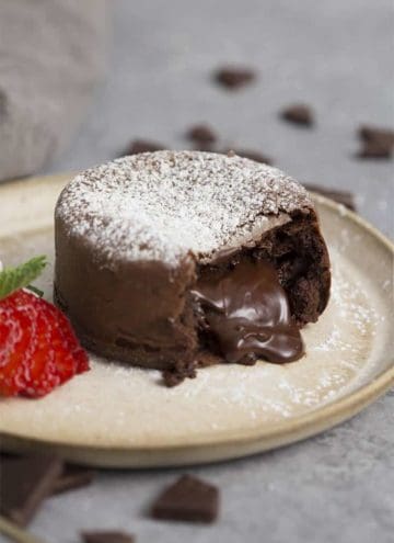 A chocolate lava cake oozing molten chocolate next to a strawberry on a taupe place