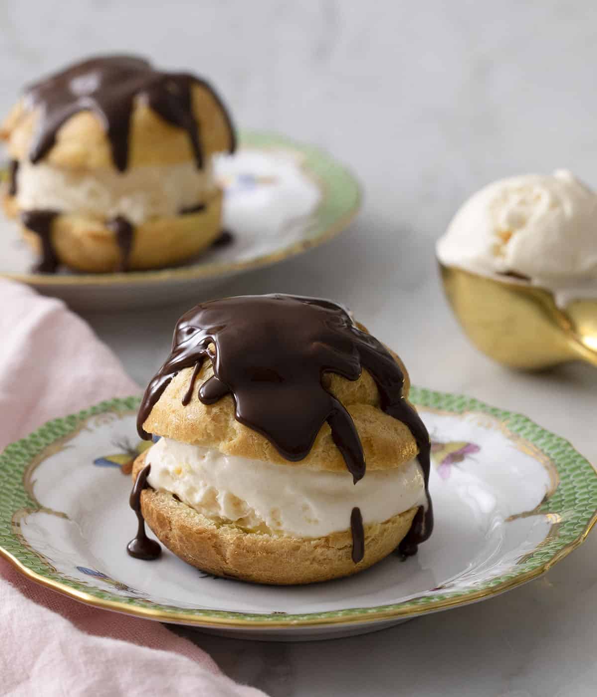 Two profiteroles filled with vanilla ice cream and topped with melted chocolate.