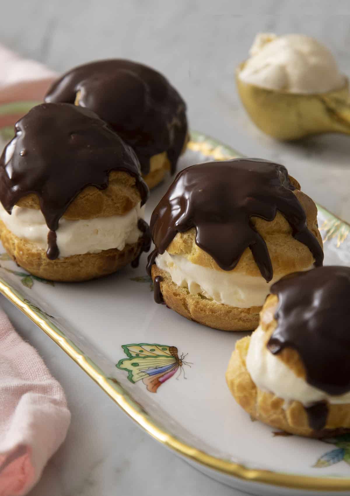 Four profiteroles topped with chocolate ganache on a serving dish.