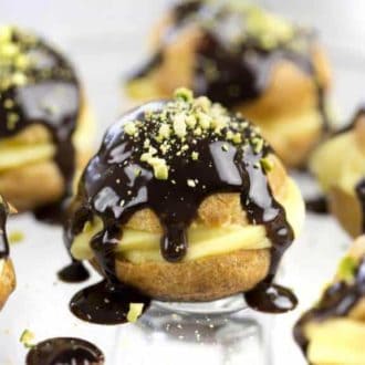 A photo of Chocolate Profiteroles topped with chocolate and chopped pistachios.