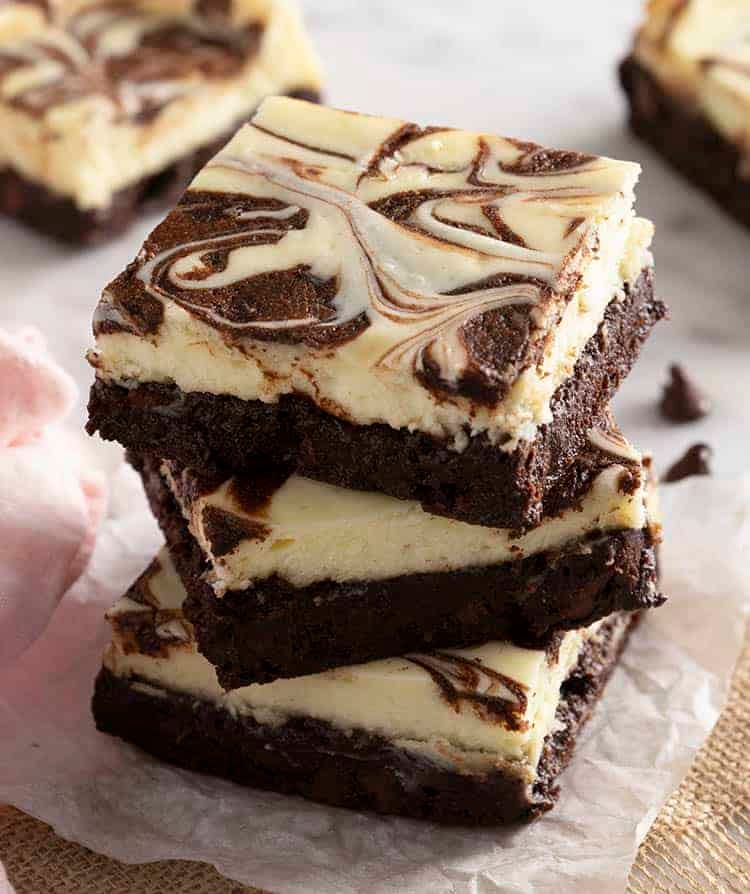 3 Cheesecake brownies stacked on a piece of parchment paper.