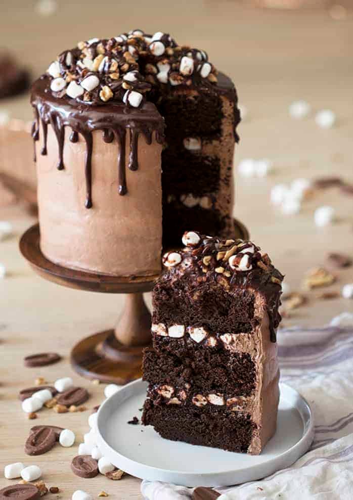 rocky road cake on a wooden cake stand with a piece in the foreground