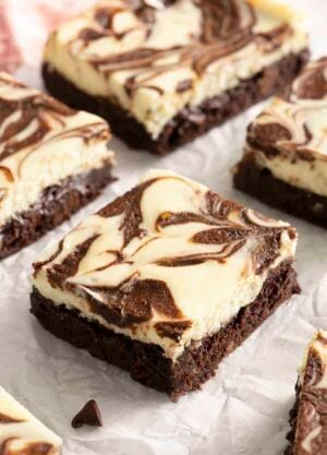 Cheesecake brownies with a chocolate swirl on parchment paper.