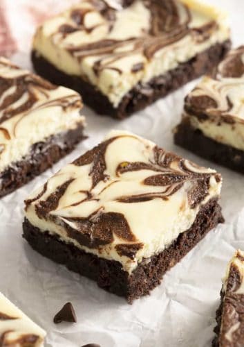 Cheesecake brownies with a chocolate swirl on parchment paper.