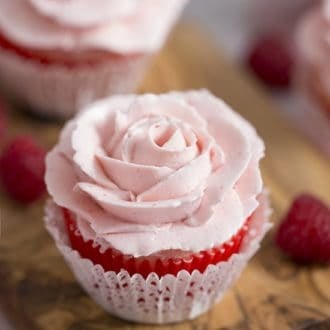 A closeup photo of a cupcake with a soft pink rose piped on top