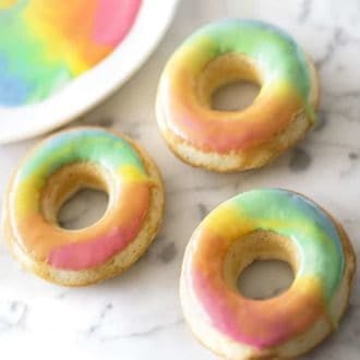 three rainbow donuts on a white marble table
