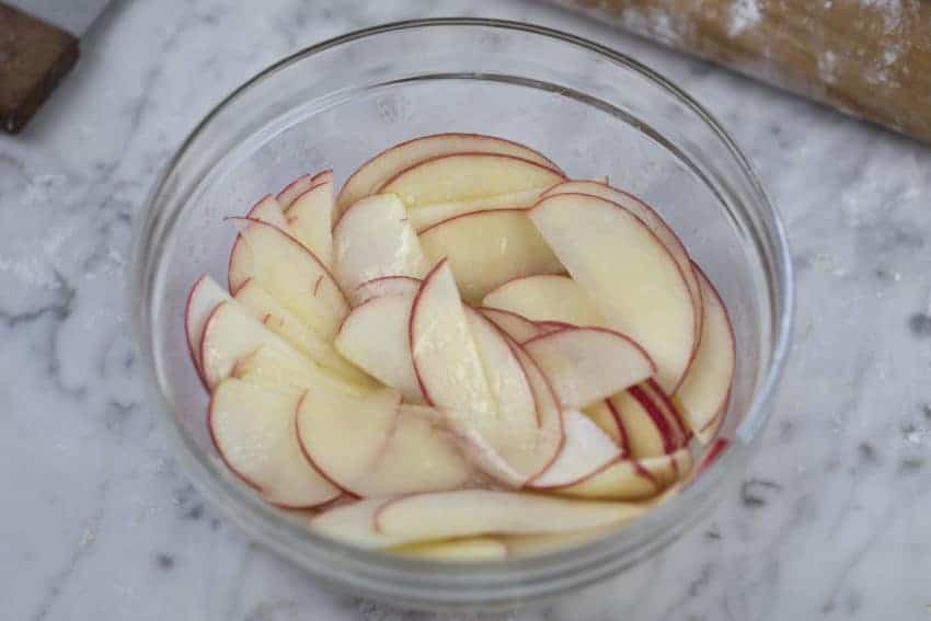 A photo of apple slices tossed in a bowl with lemon butter and sugar.