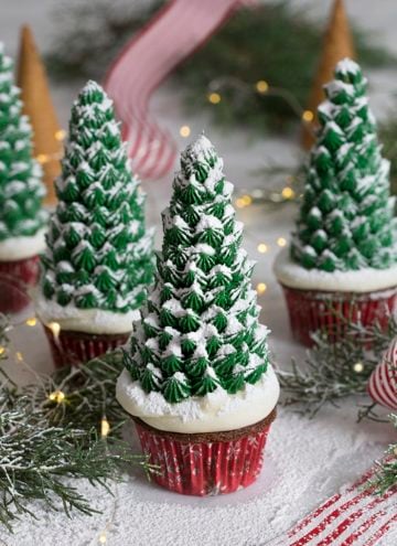A photo of a group of Christmas tree cupcakes surrounded by evergreen branches