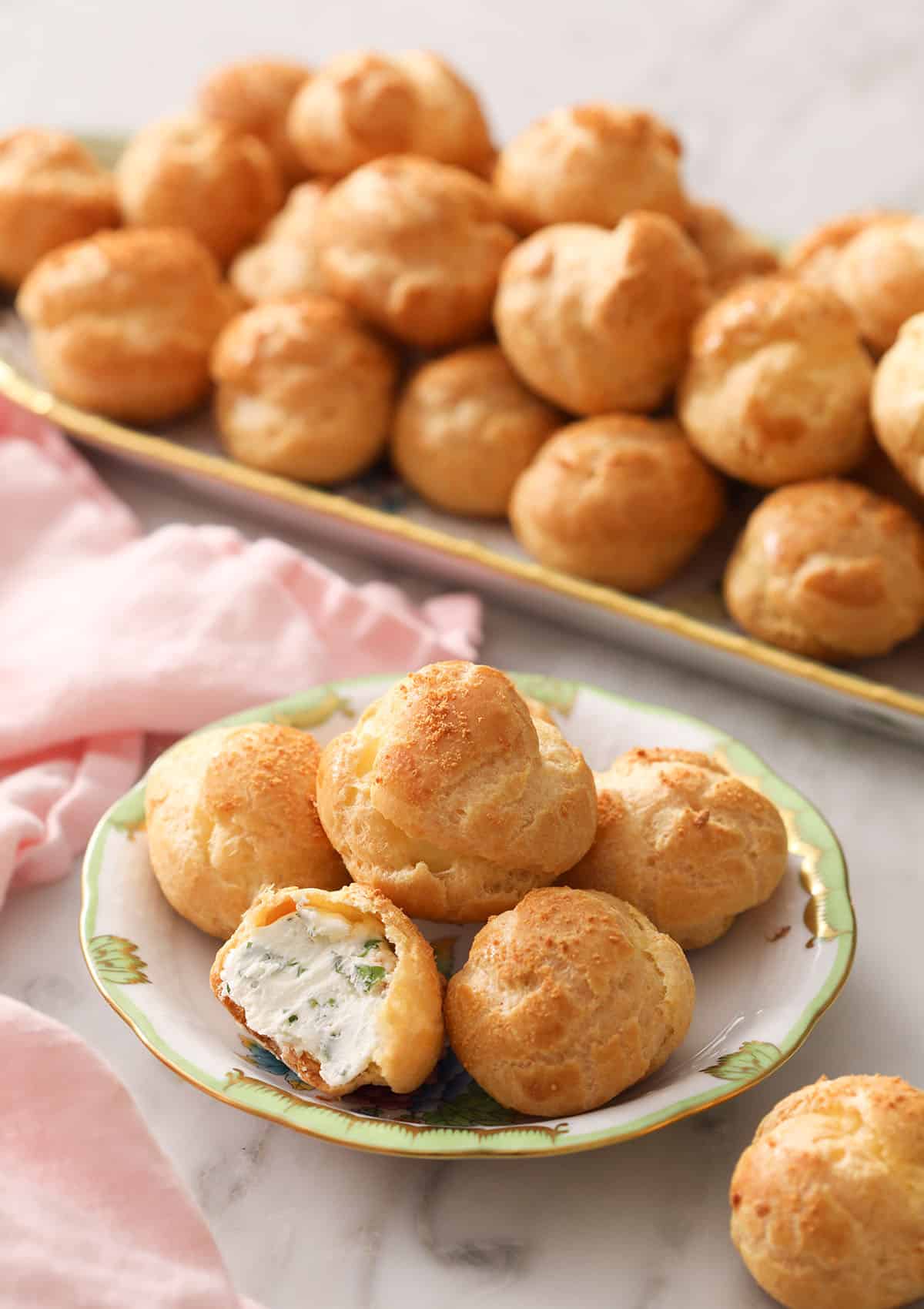 Cheese puffs on a small plate in front of a serving tray full of them
