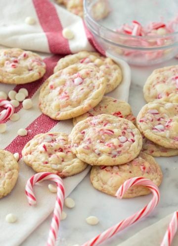 A photo of white chocolate peppermint cookies on a marble table surrounded by candy canes