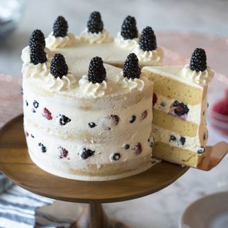 A photo showing a mascarpone berry cake on a wooden cake stand with a piece being removed