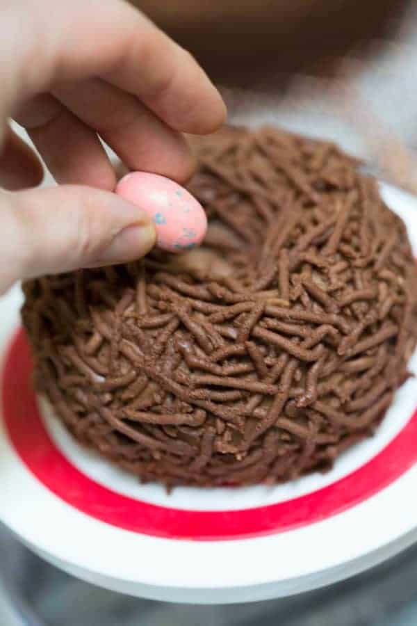A photo of a bird's nest cake with the chocolate eggs being placed in the center