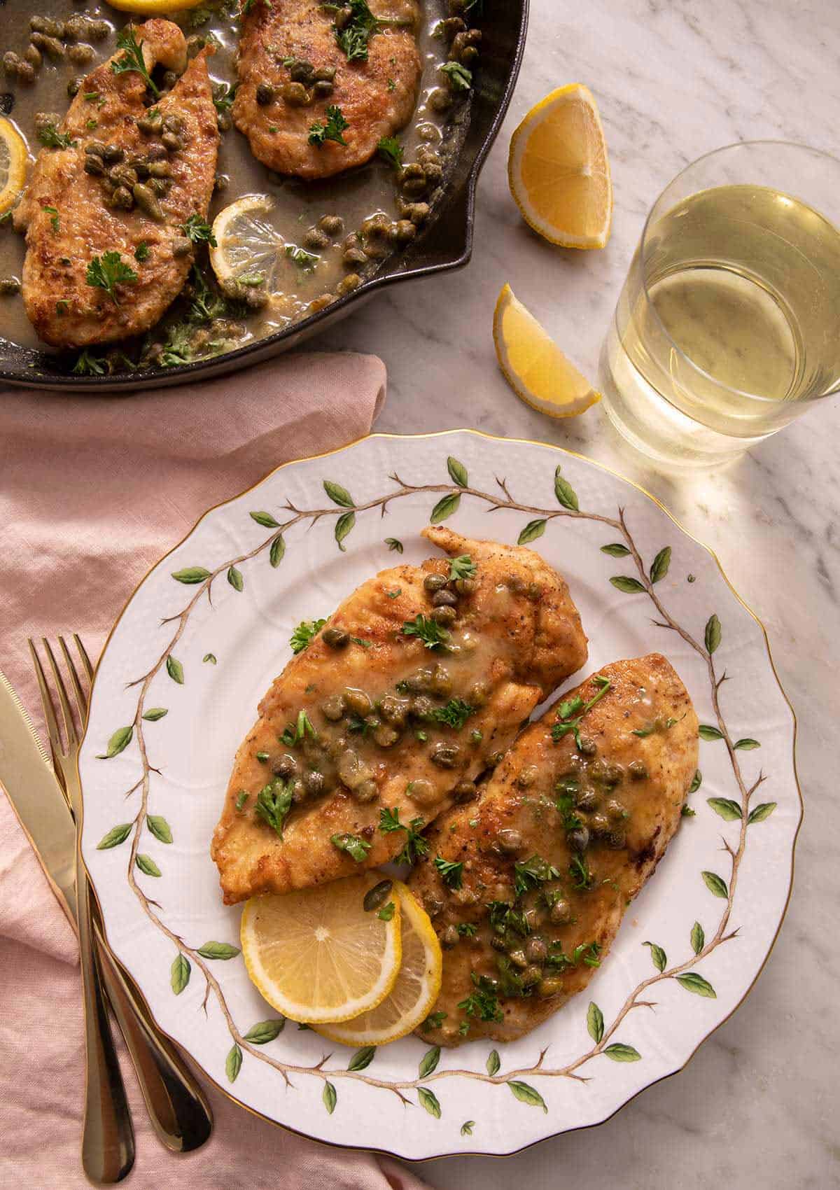 Overhead view of a plate with two servings of chicken piccata by a glass of wine.