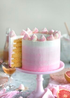 A photo of a champagne grapefruit cake on a pink cake stand with a piece being removed.