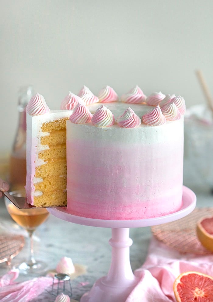 A photo of a champagne grapefruit cake on a pink cake stand with a piece being removed.