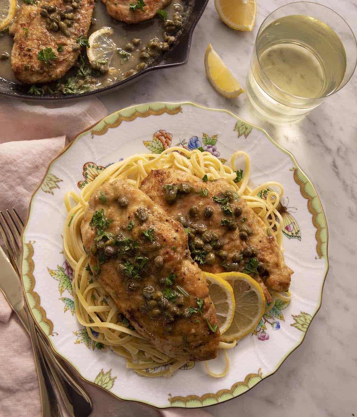 Overhead view of chicken piccata in a plate over noodles.