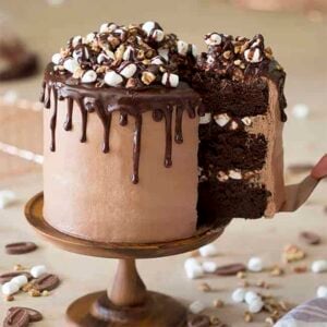 A Rocky Road Cake on a wooden cake stand with a lift lifted out.