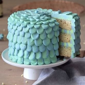 A three layer bluegreen cake on a white cake stand