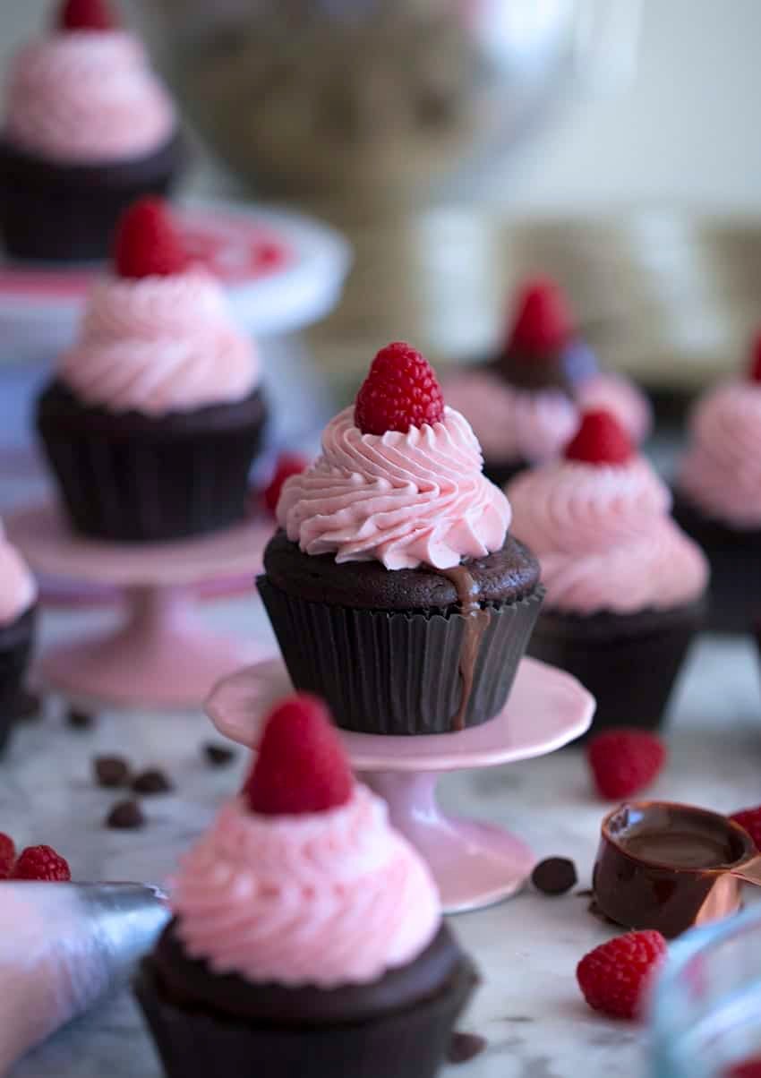 Photo of a group of chocolate cupcakes with pink raspberry buttercream and a raspberry on top.