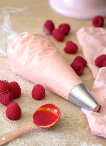 A piping bag filled with raspberry buttercream with berries scattered around