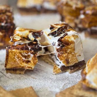 A large homemade s'more pulled in half on a table covered in powdered sugar