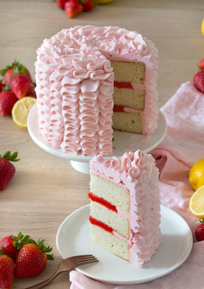 A photo of a pink Strawberry Lemonade Cake with a piece being removed