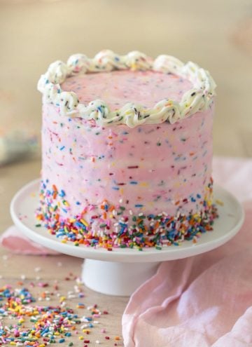 A pink funfetti cake on a white cake stand