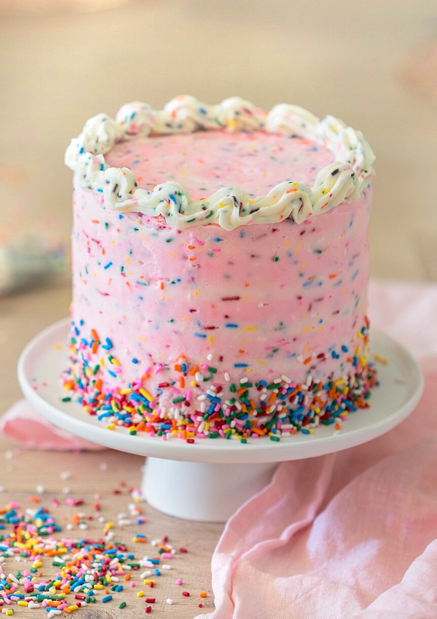 A pink funfetti cake on a white cake stand