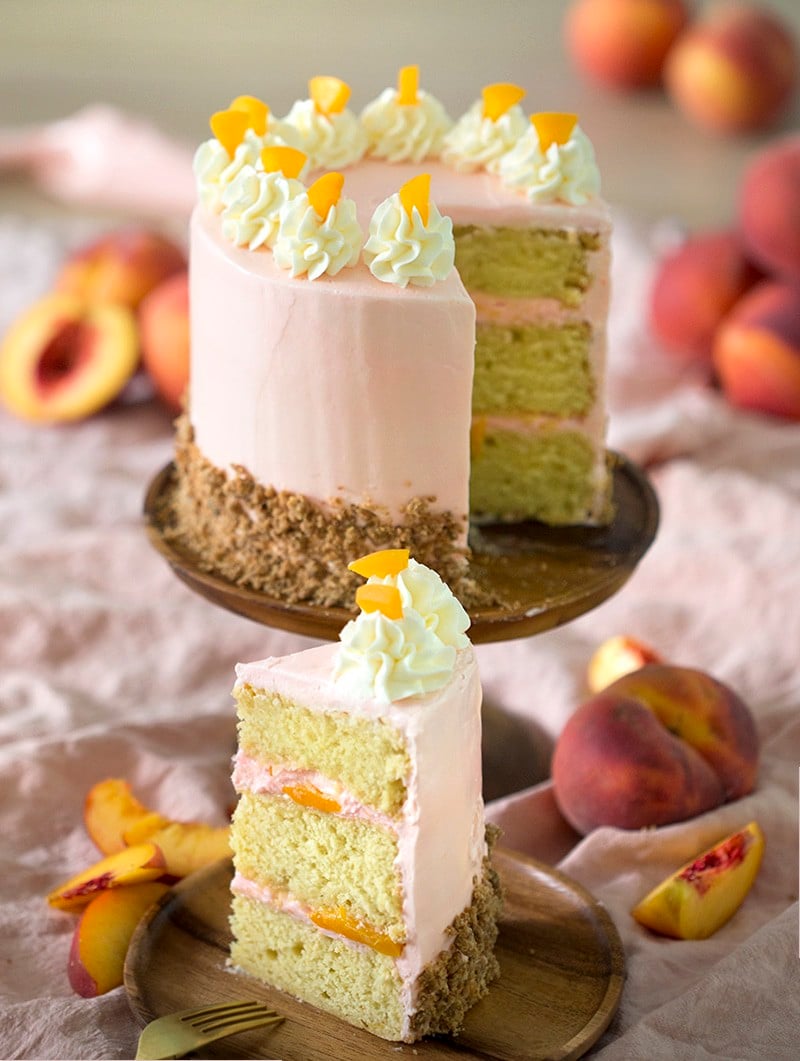 A slice of soft pink peach cake on a wooden plate.
