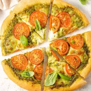 An overhead shot of a pesto pizza cut into slices