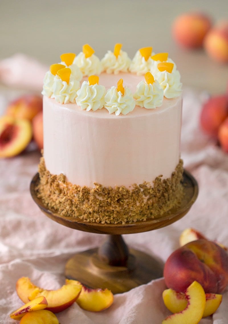 A photo of a peach cake on a wooden cake stand surrounded by peach slices.