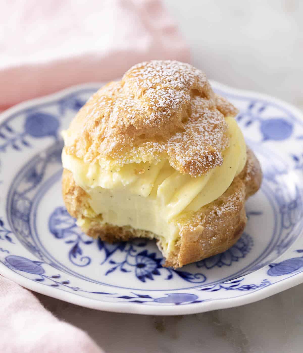 Close up of a cream puff on a plate with a bite taken out.