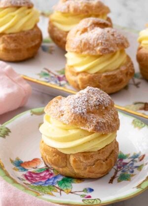A cream puff with a dusting of powdered sugar on a plate in front of a platter.