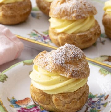 A cream puff with a dusting of powdered sugar on a plate in front of a platter.