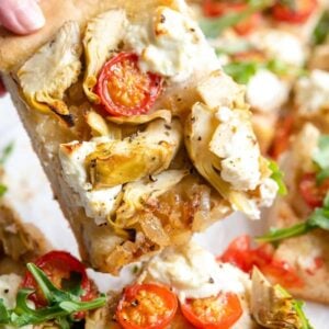 A slice of artichoke pizza lifted up.